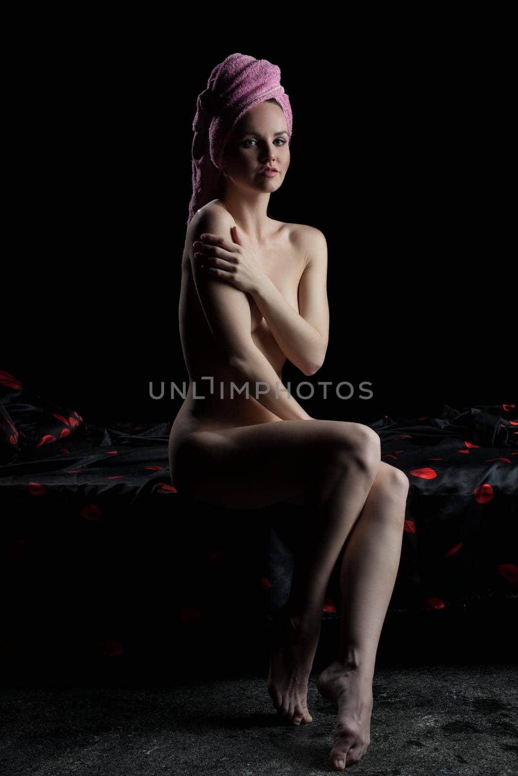 Full length portrait of sexy young woman sitting on bed in dark bedroom