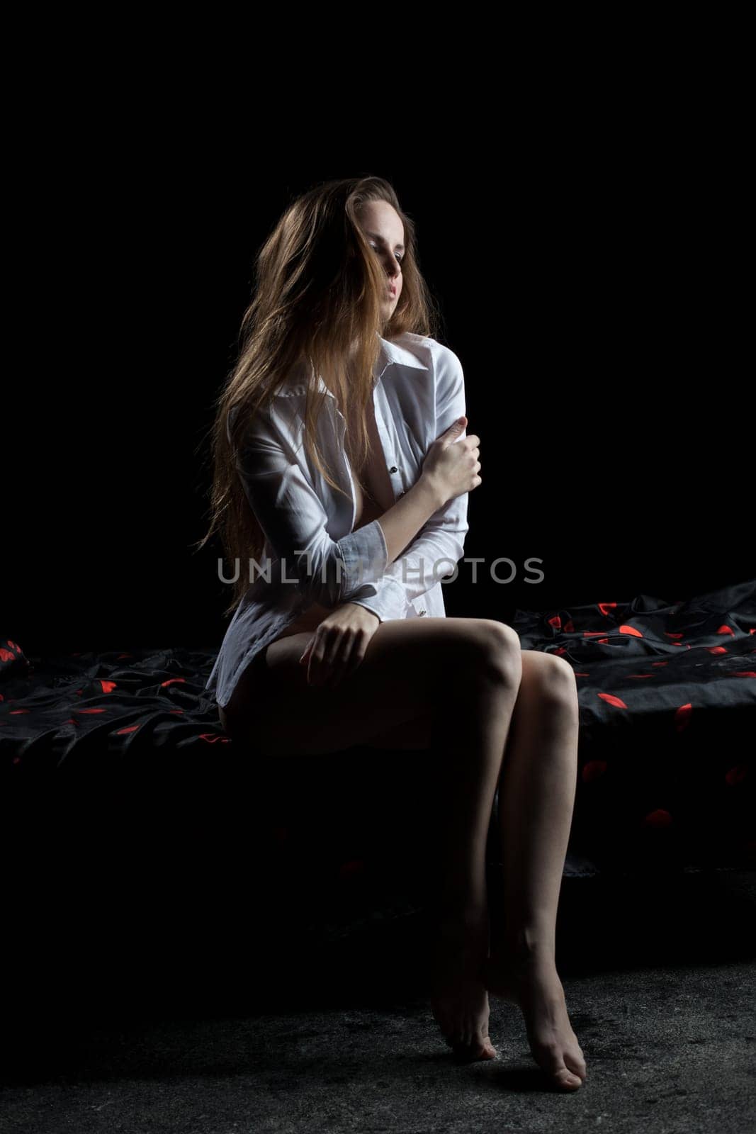 Full length portrait of sexy woman sitting on bed in dark bedroom