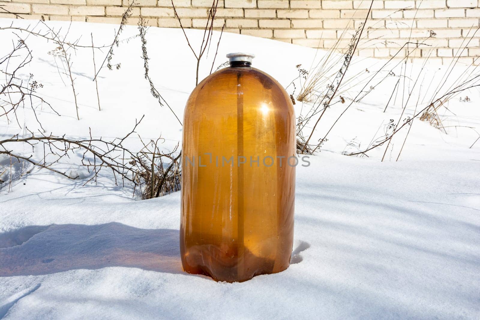 a large dark plastic bottle of juice or beer in the snow