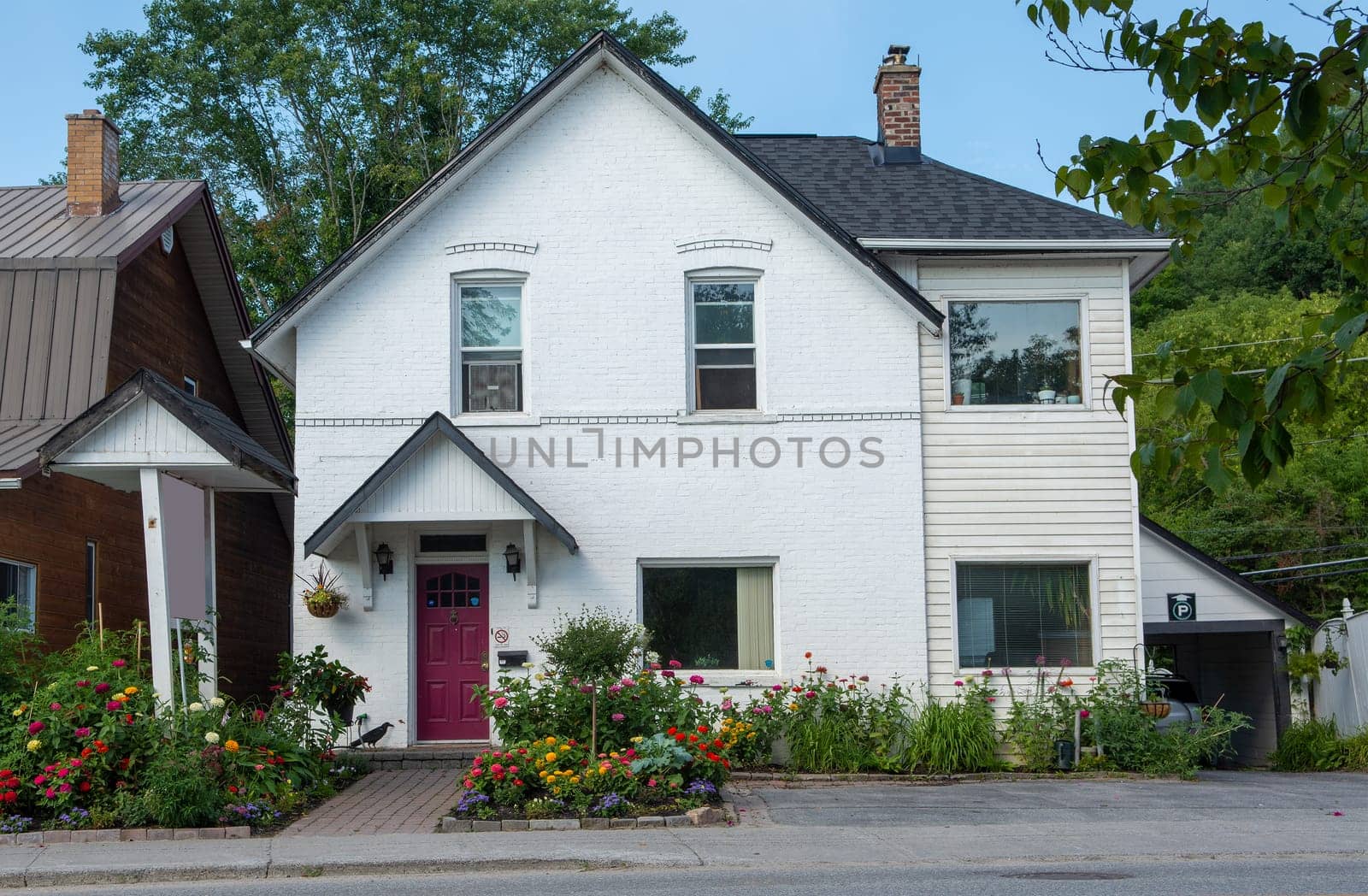 The facade of a small house is decorated with flower beds with colorful flowers.