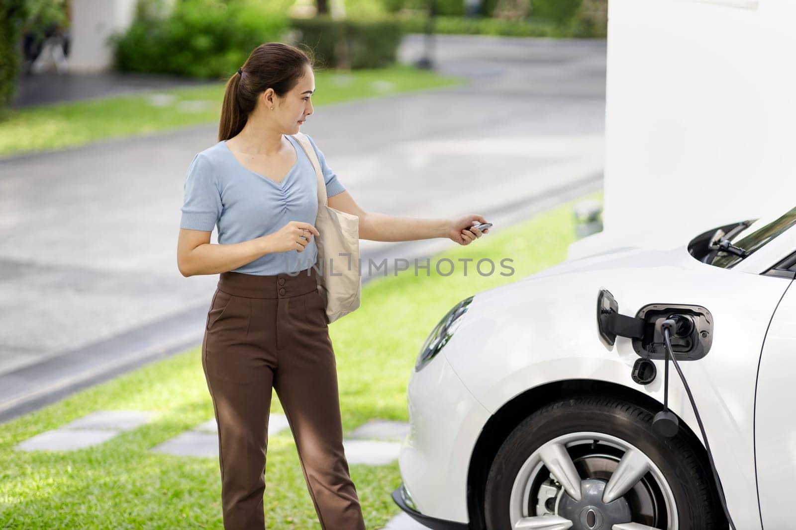 Progressive woman install cable plug to her electric car with home charging station. Concept of the use of electric vehicles in a progressive lifestyle contributes to clean environment.