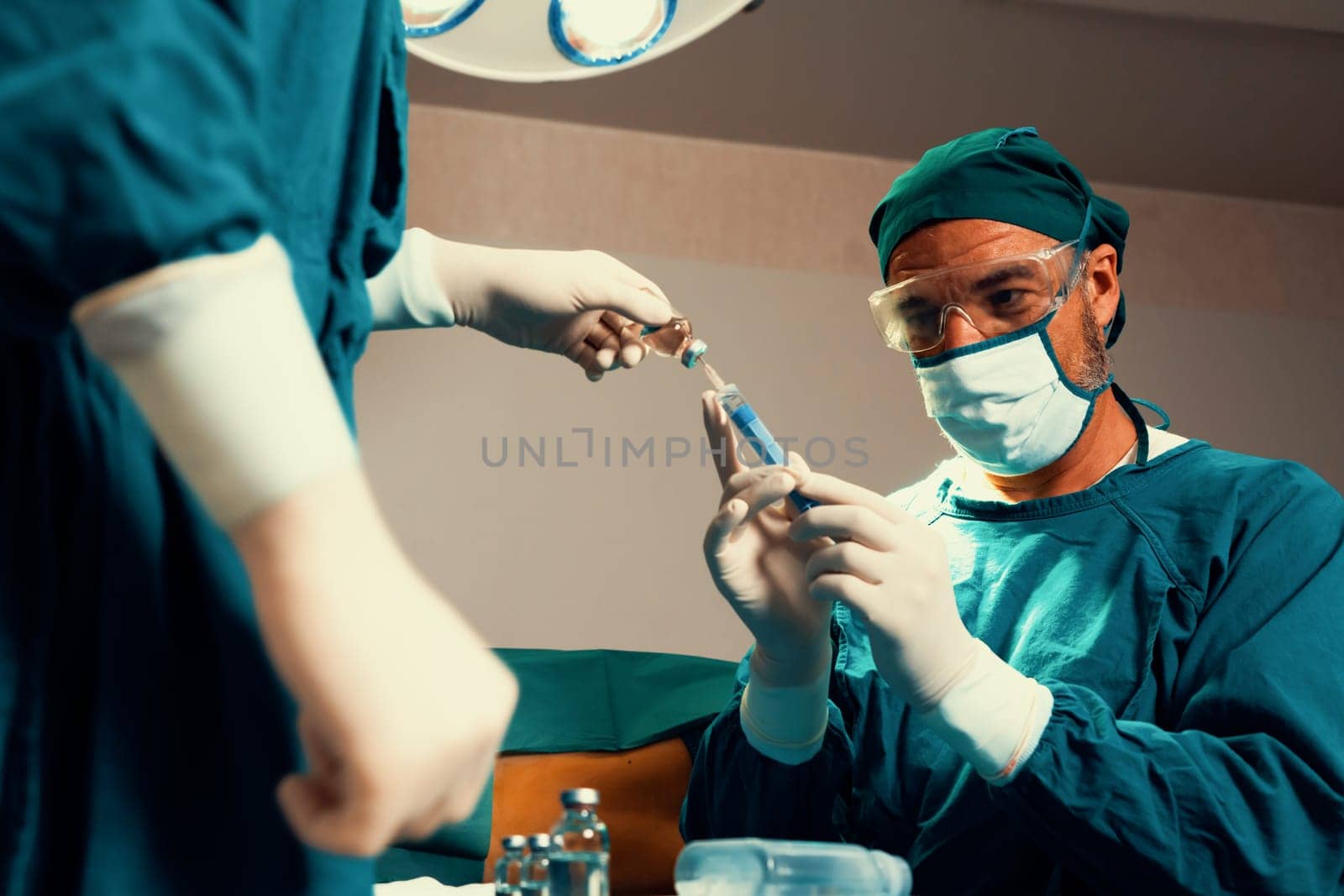 Surgeon fill syringe from medical vial for surgical procedure at sterile operation room with assistance nurse. Doctor and medical staff in full protective wear for surgery prepare anesthesia injection