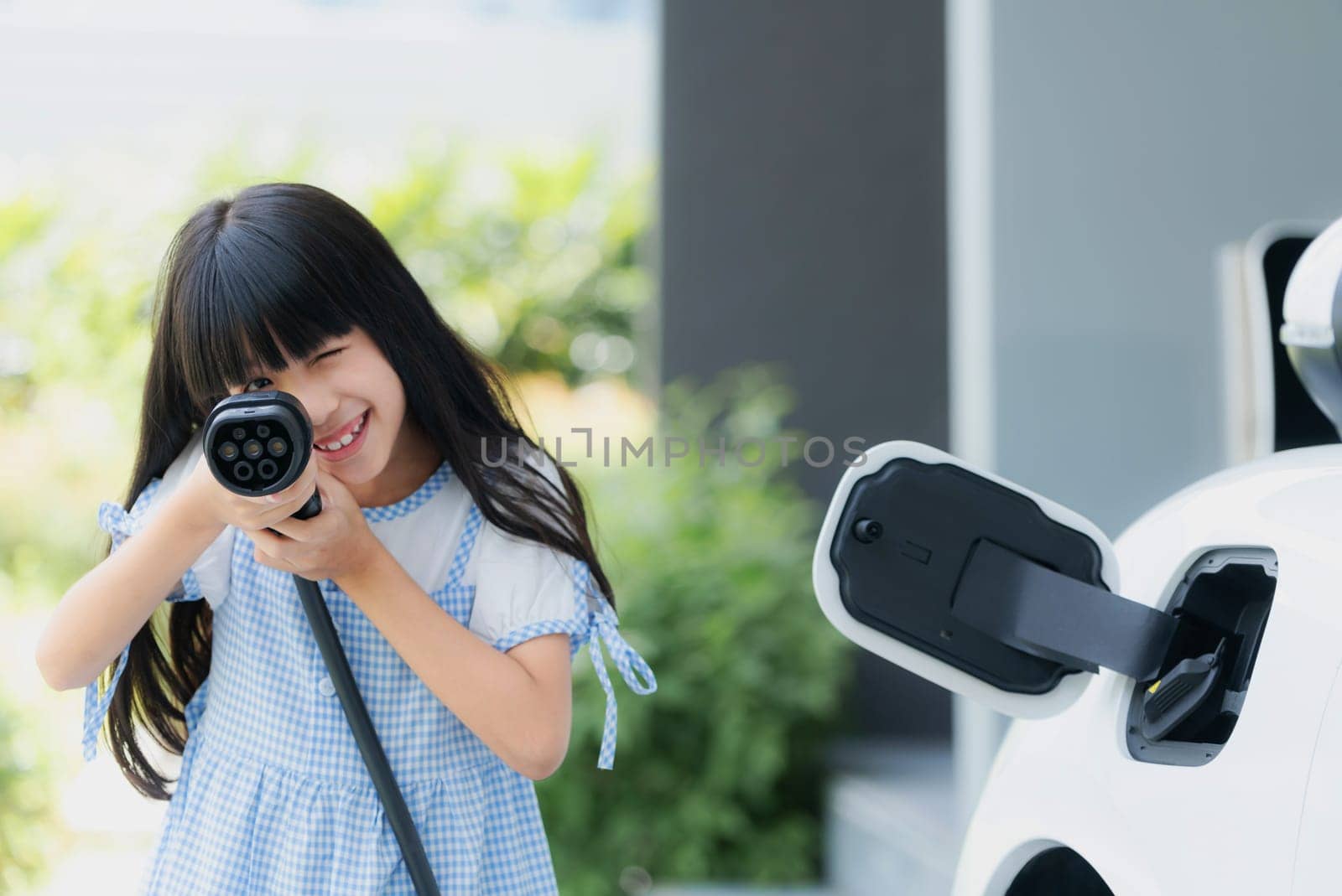 A playful girl holding and pointing an EV plug, a home charging station providing a sustainable power source for electric vehicles. Concept of progressive new generation with ecological awareness.