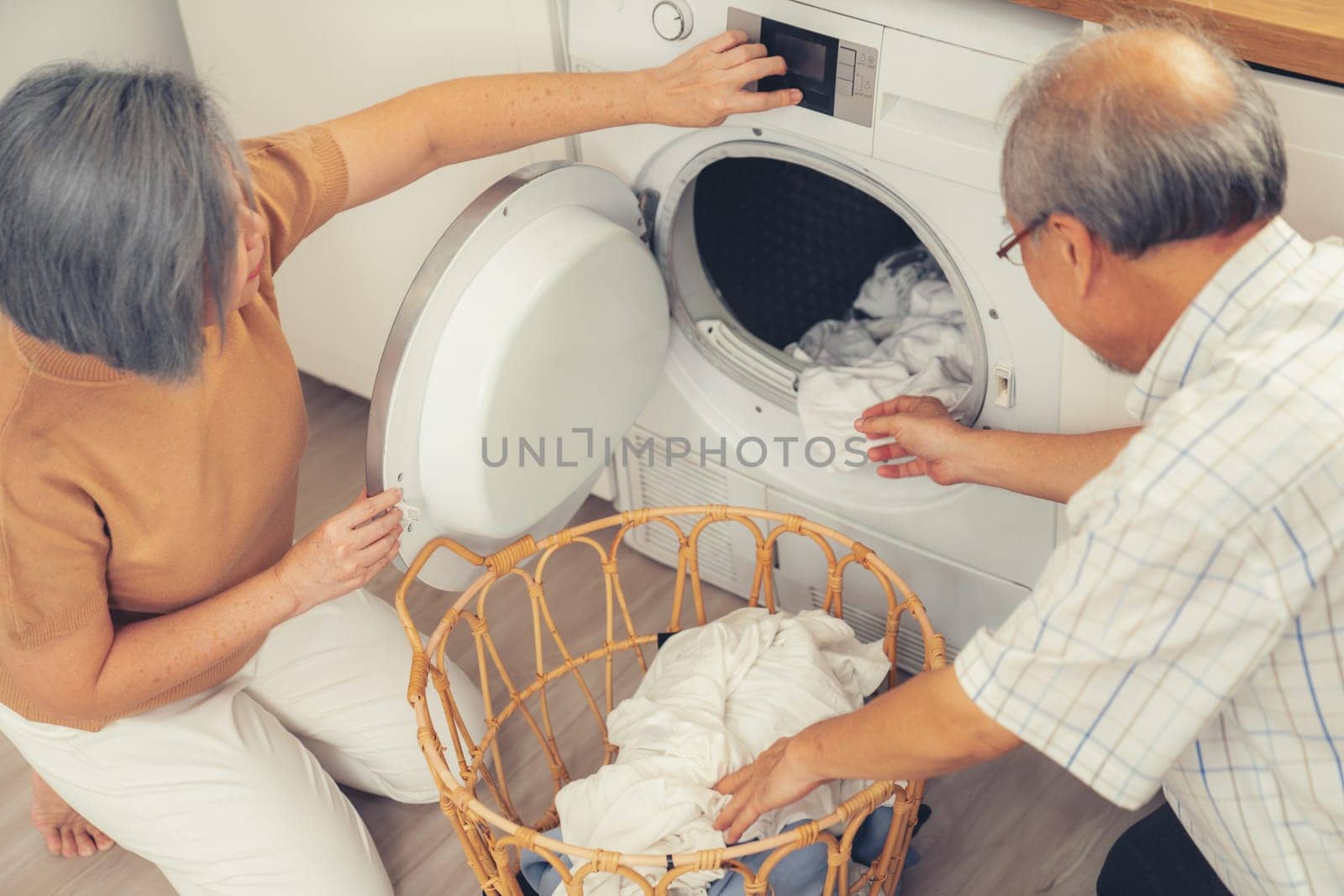 Senior couple working together to complete their household chores at the washing machine in a happy and contented manner. Husband and wife doing the usual tasks in the house.