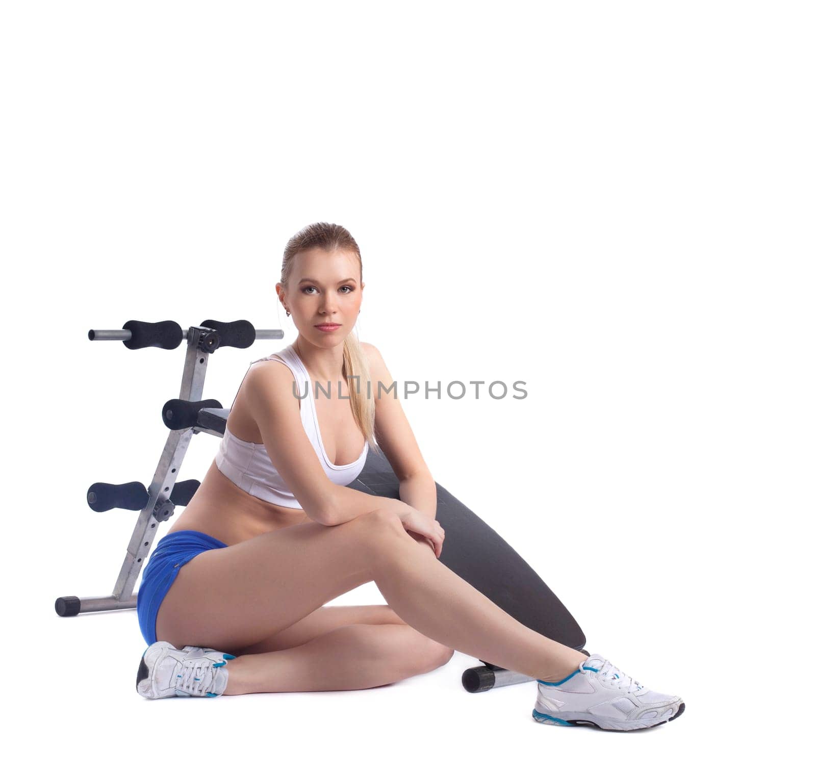 Young blonde woman near exerciser. Isolated on white