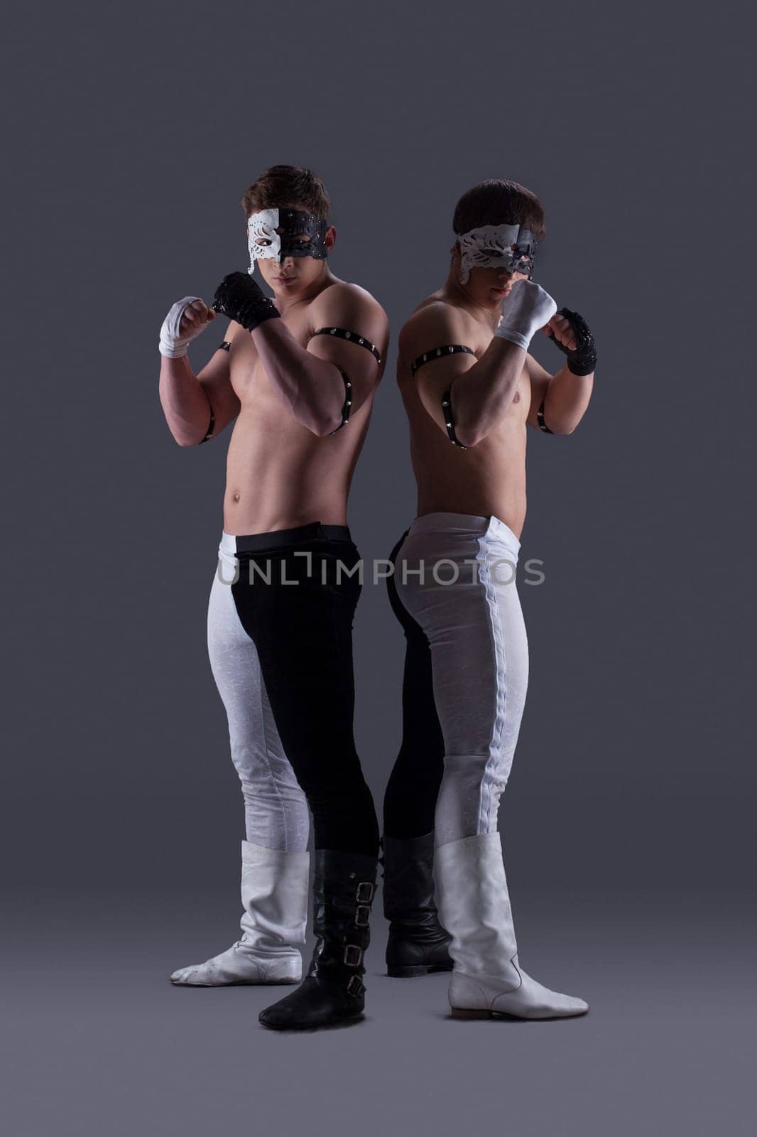 Two attractive men in masks posing in studio, on gray background