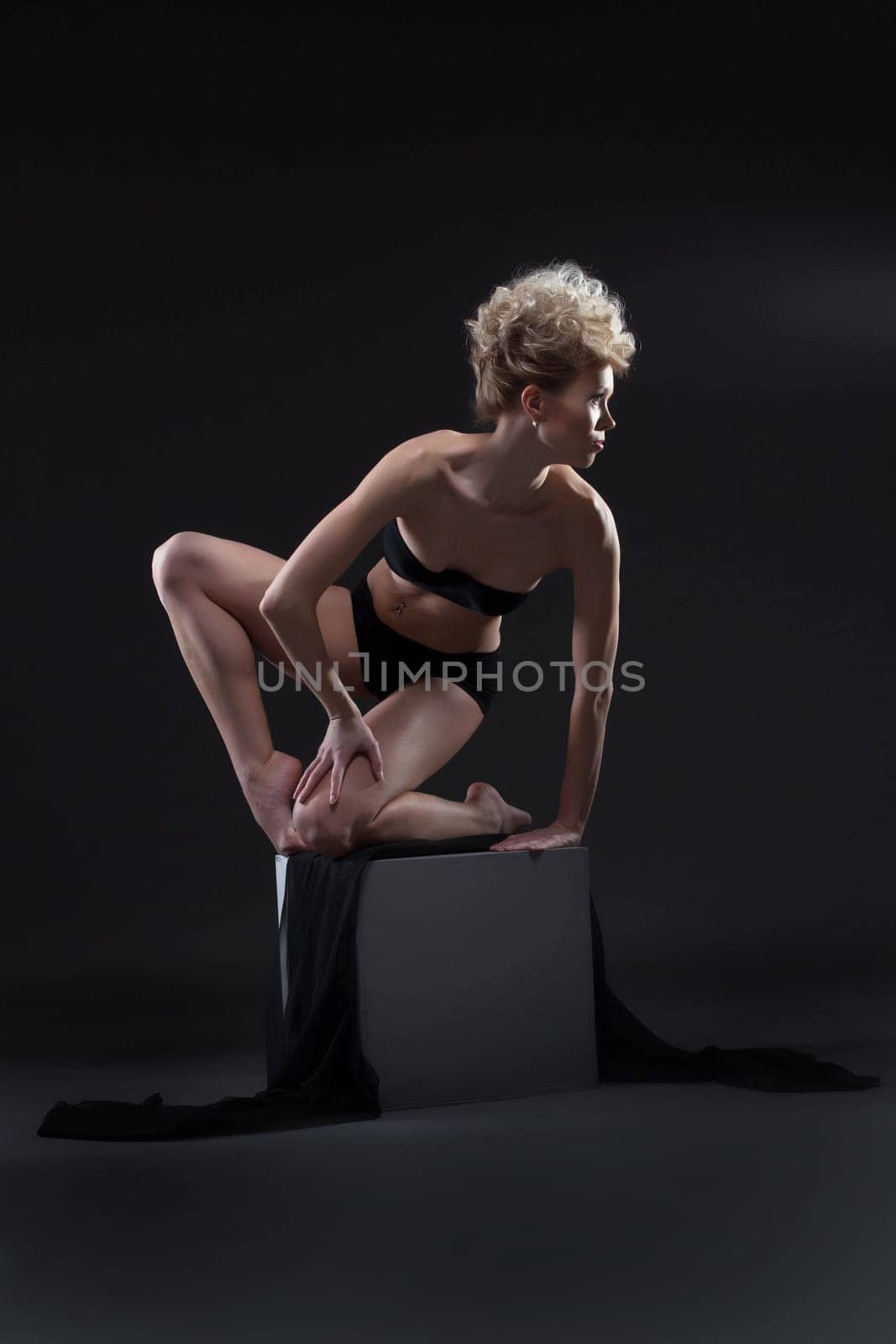 Elegant curly blonde posing on cube in studio