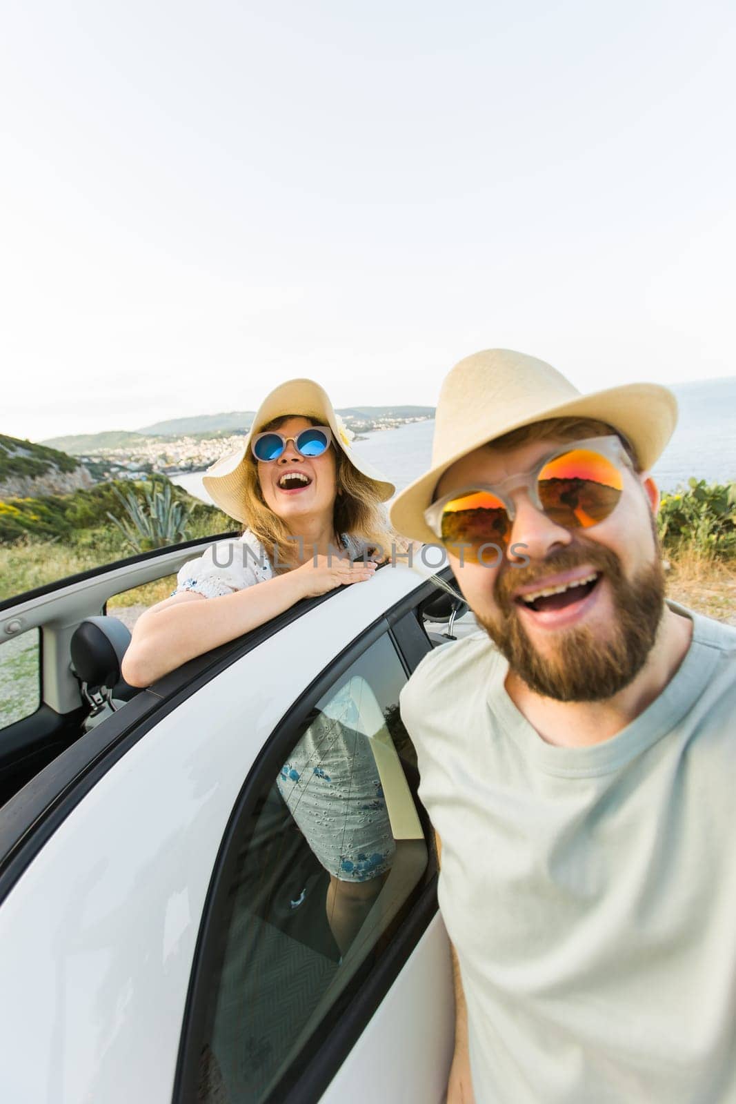 Romantic couple making selfie on smartphone camera in rental cabrio car on ocean or sea beach enjoying summer vacation together and taking picture on cellular resting near sea on weekends by Satura86