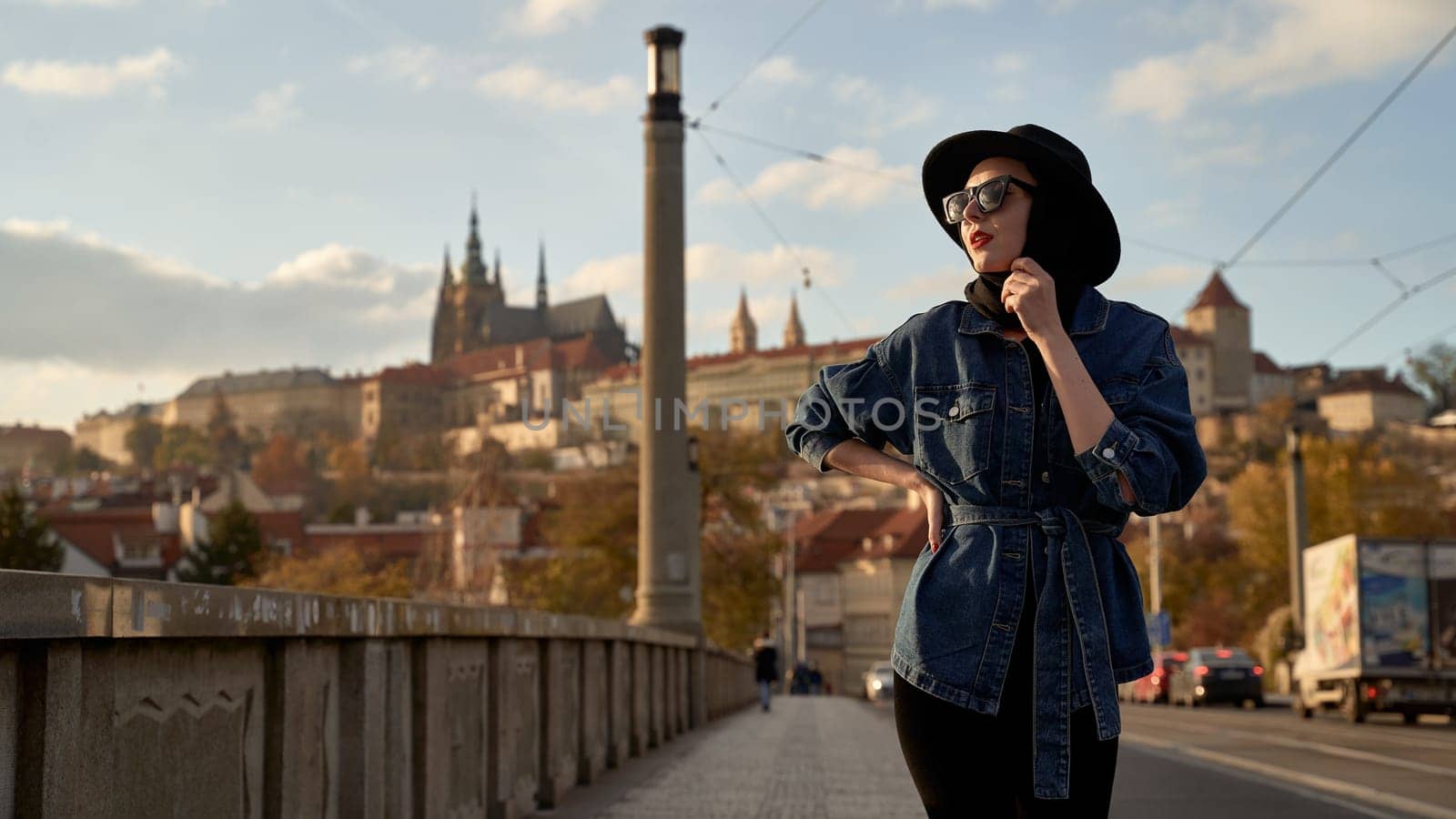 Stylish beautiful young woman earing black hat in Prague on a bridge with Prague Castle or Prazsky Hrad on background. Elegant retro lady fine art portrait. by berezko