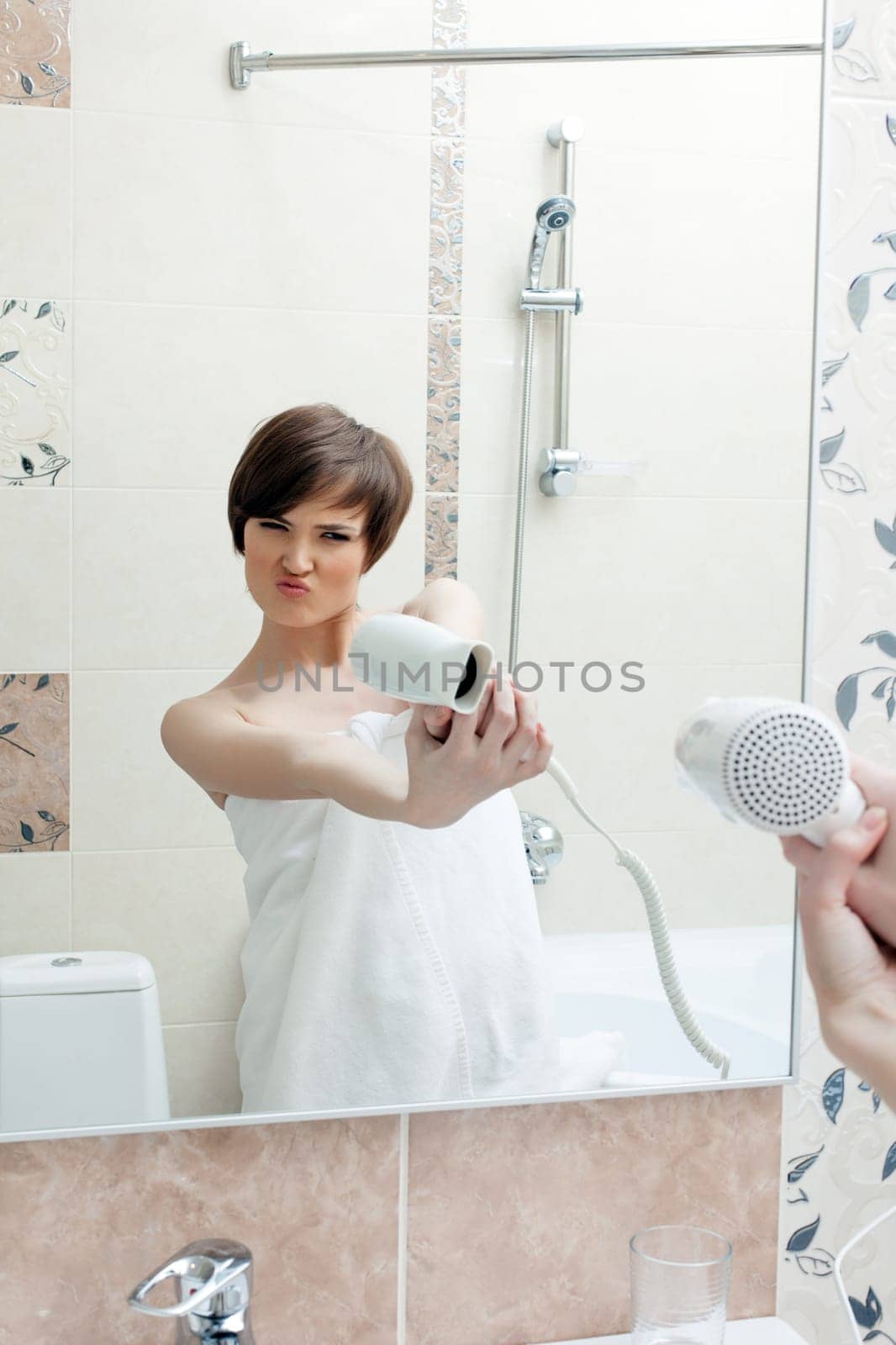 Playful girl posing with hair dryer, in hotel bathroom