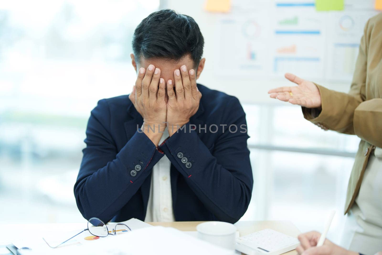 An image of an Asian male employee looking worried and sad about being scolded by his boss for failing to meet sales targets, concept of disappointment and failure in his career.