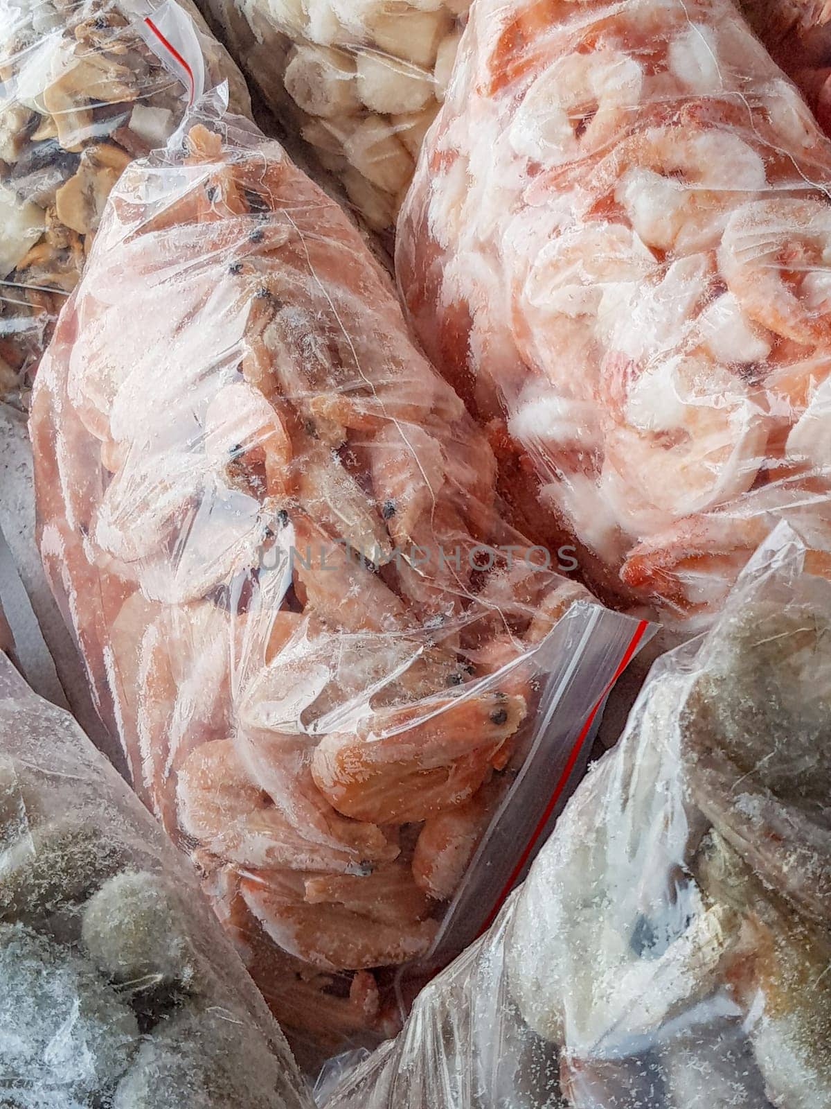 There are many large plastic bags with frozen raw and boiled shrimp on the counter of the fish market