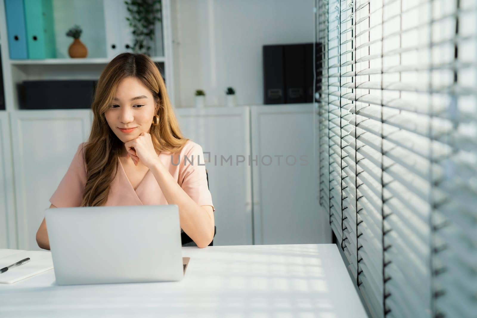 A young Asian female employee sitting at her desk in her office, sitting at desktop in workstation.