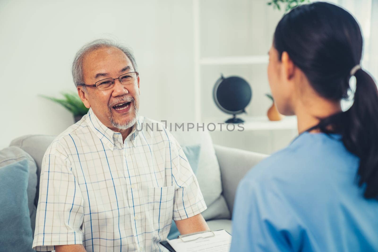 Caring young female doctor examining her contented senior patient with stethoscope in living room. Medical service for elderly, elderly sickness, declining health.