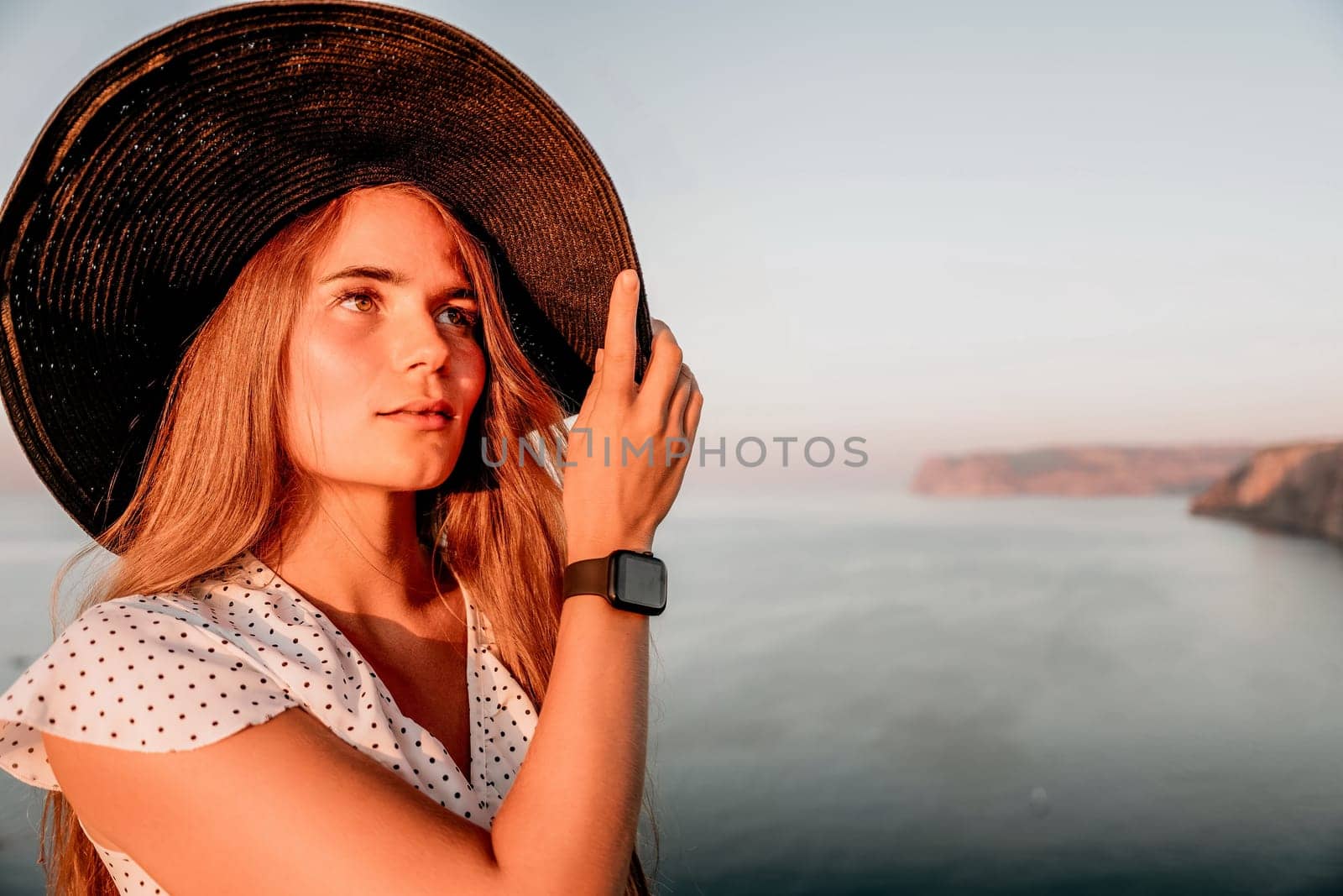 Portrait of happy young woman wearing summer black hat with large brim at beach on sunset. Closeup face of attractive girl with black straw hat. Happy young woman smiling and looking at camera at sea