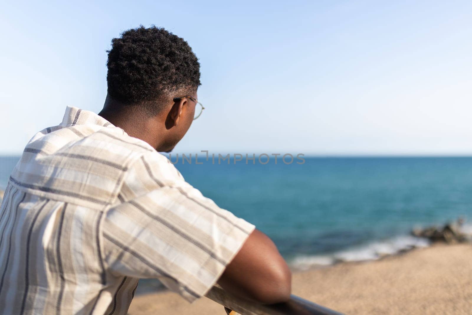Rear view of pensive african american man relaxing looking at the ocean. Copy space. Vacation concept.