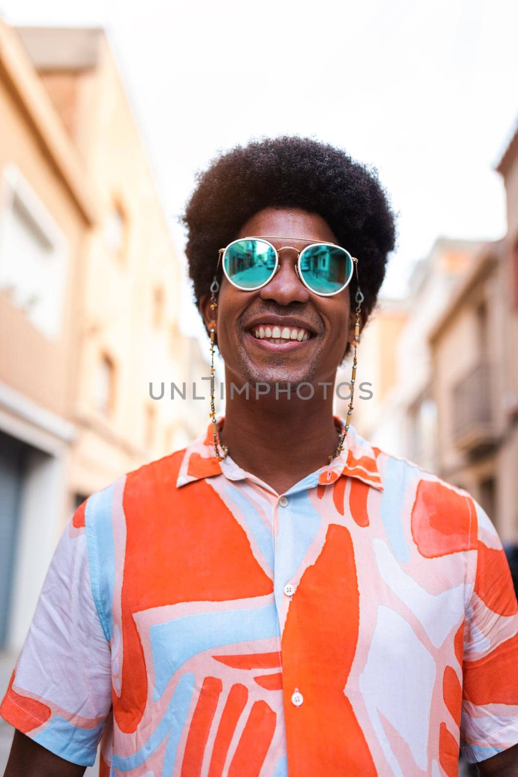 Vertical portrait of young happy and smiling black man wearing sunglasses outdoors. by Hoverstock