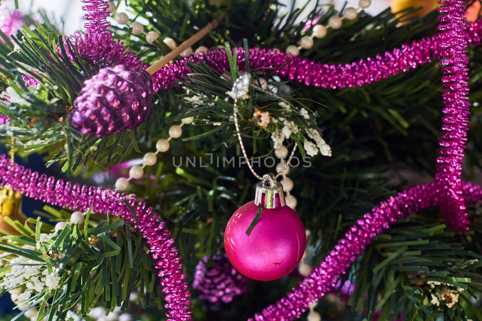 Decoration of an artificial Christmas tree for the holiday. Pink plastic ball and pink tinsel. New Year.