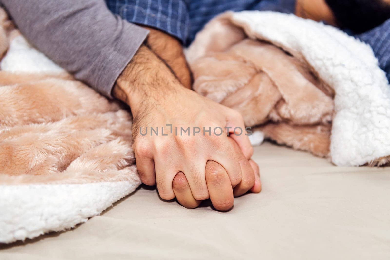 detail of the hands of an unrecognizable couple of gay men linked on the bed, concept of real people lifestyle and love between people of the same sex