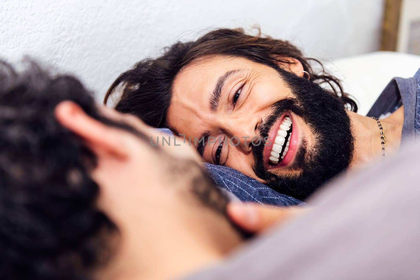 smiling happy man relaxed in bed stroking his boyfriend's face, concept of real people lifestyle at home and love between people of the same sex