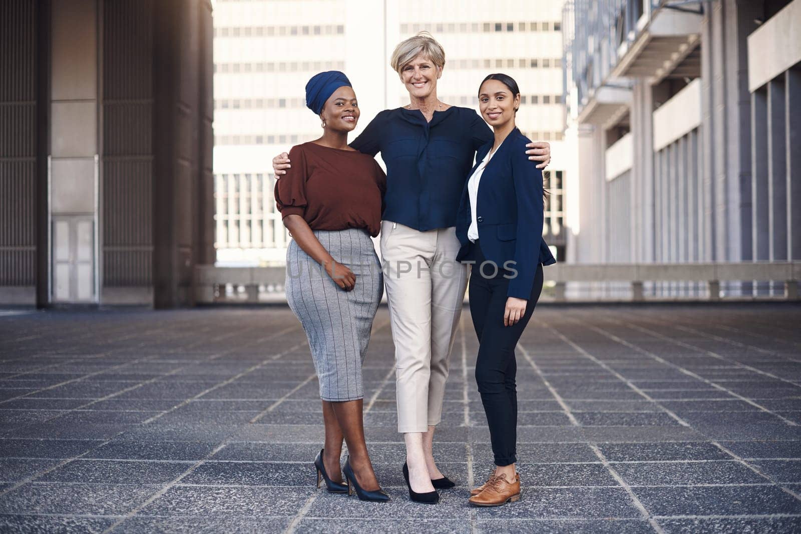 Our team is our source of strength. Portrait of a group of businesswomen standing together against a city background. by YuriArcurs