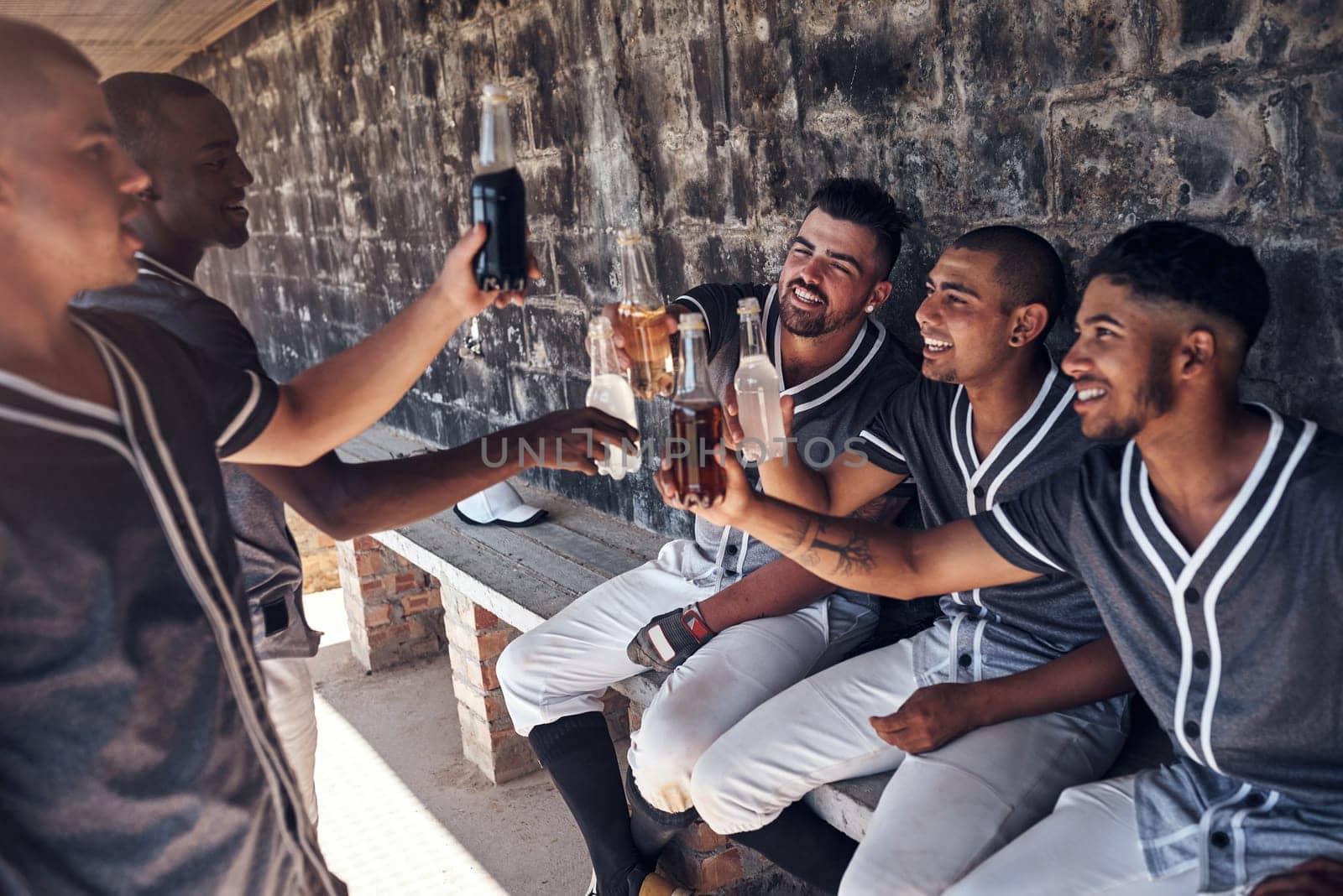 Cheers to the champs. a group of young men celebrating with drinks after playing a baseball game. by YuriArcurs