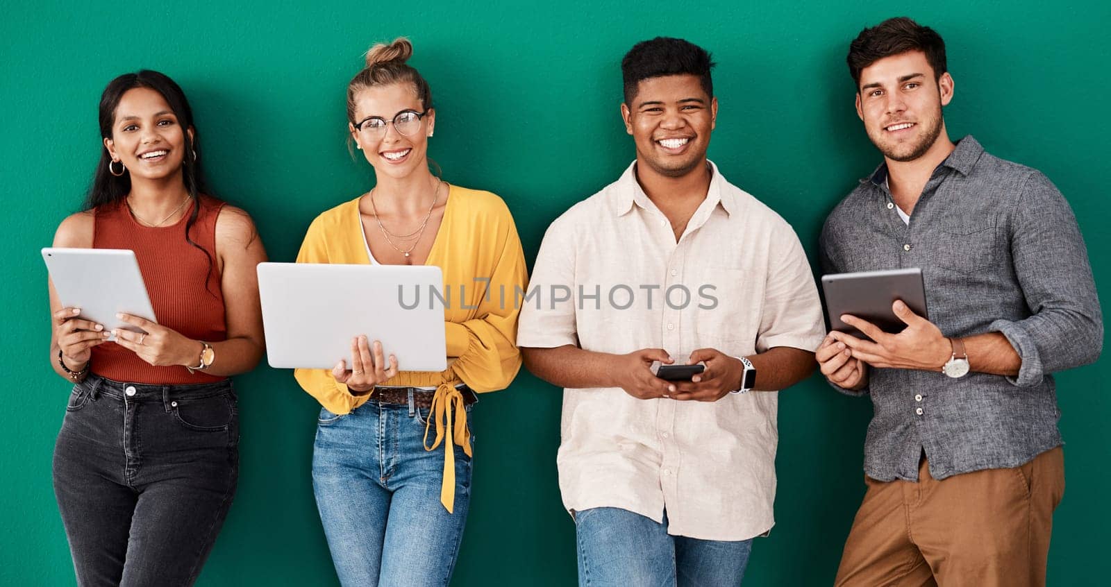 We use social media to connect and engage with customers. Portrait of a group of young designers using digital devices while standing together against a green background. by YuriArcurs