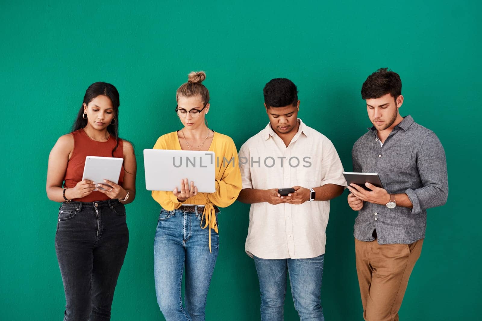 Staying connected to their online and mobile channels. a group of young designers using digital devices while standing together against a green background. by YuriArcurs