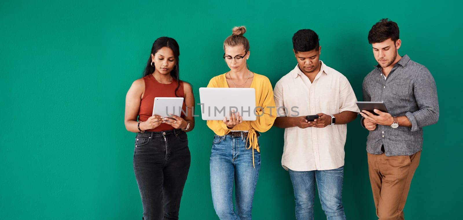Stay connected to your office with the right business tools. a group of young designers using digital devices while standing together against a green background. by YuriArcurs