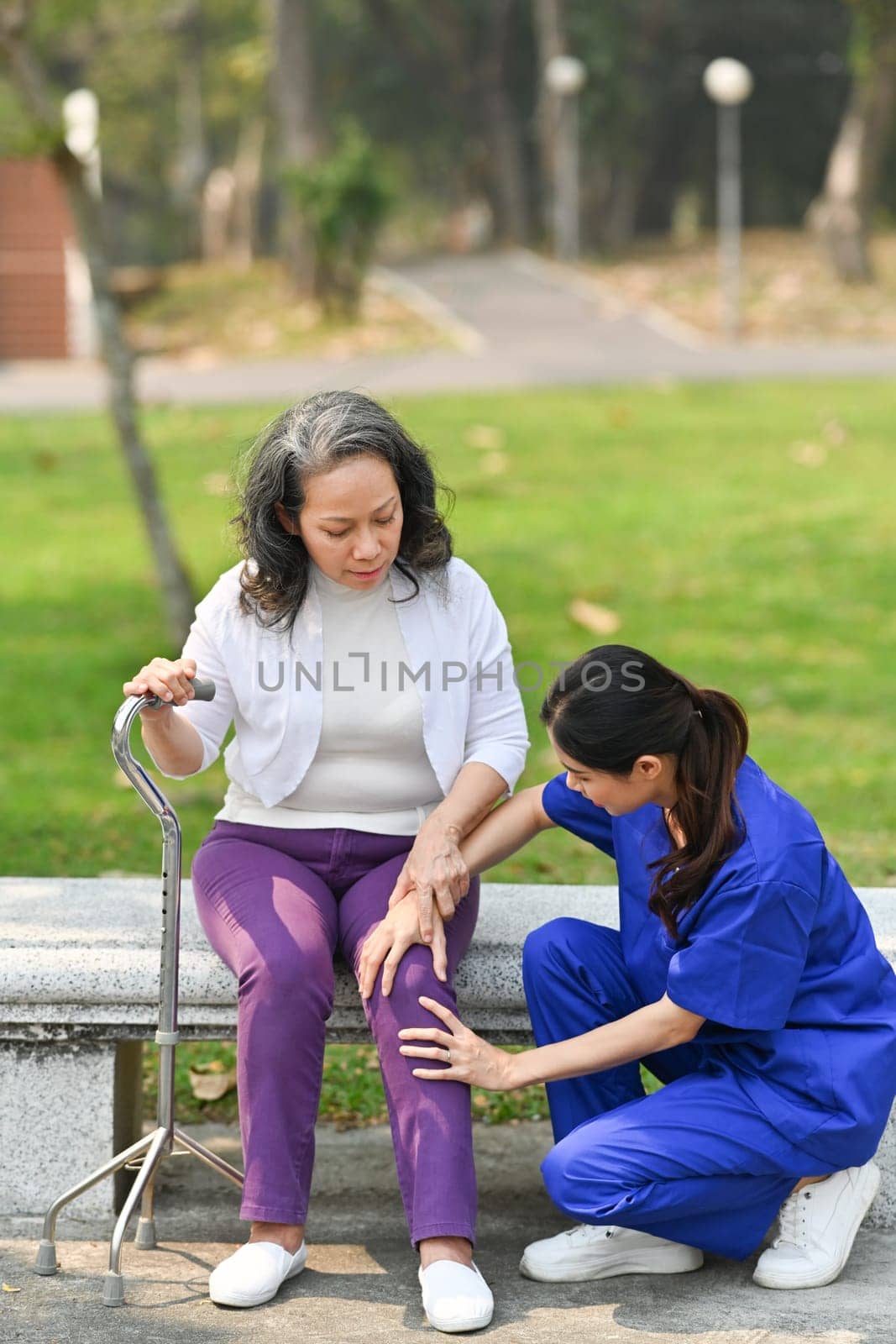 Positive female nurse in uniform taking care of senior woman in the garden at home care. Assistance, rehabilitation concept.
