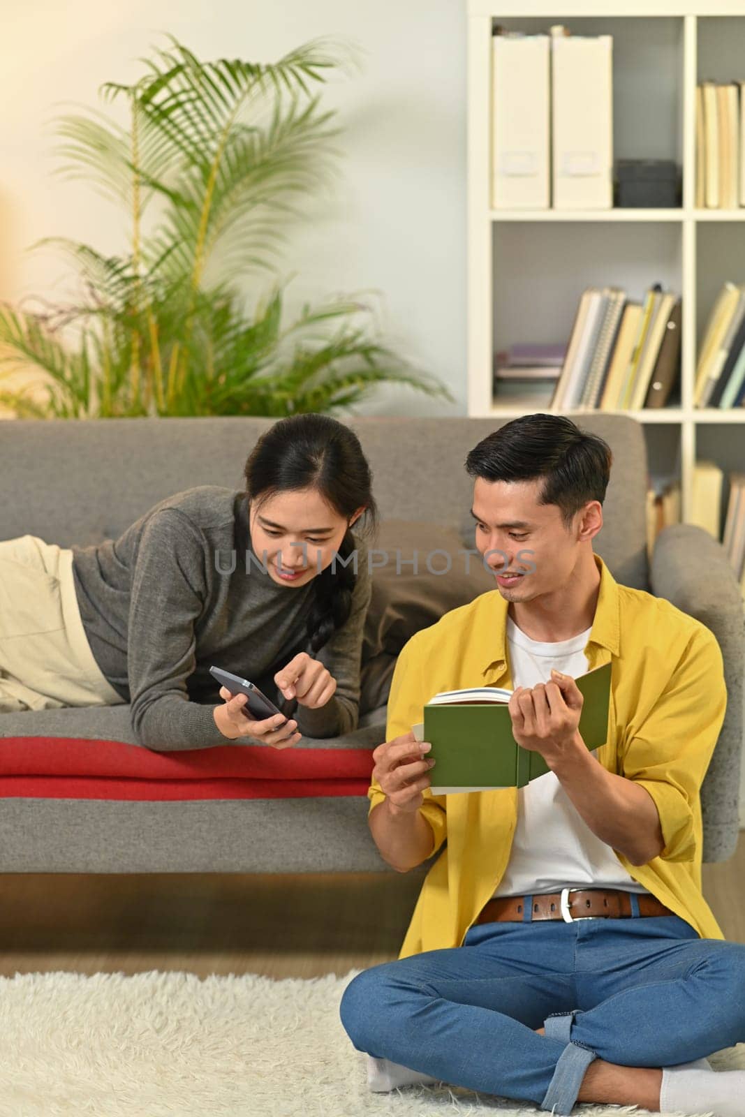 Happy married young couple reading book, enjoying leisure time on weekend at home.