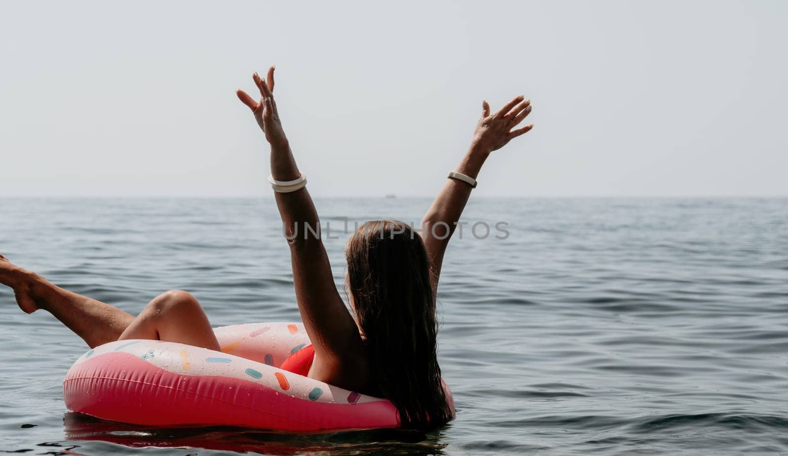 Woman summer sea. Happy woman swimming with inflatable donut on the beach in summer sunny day, surrounded by volcanic mountains. Summer vacation concept