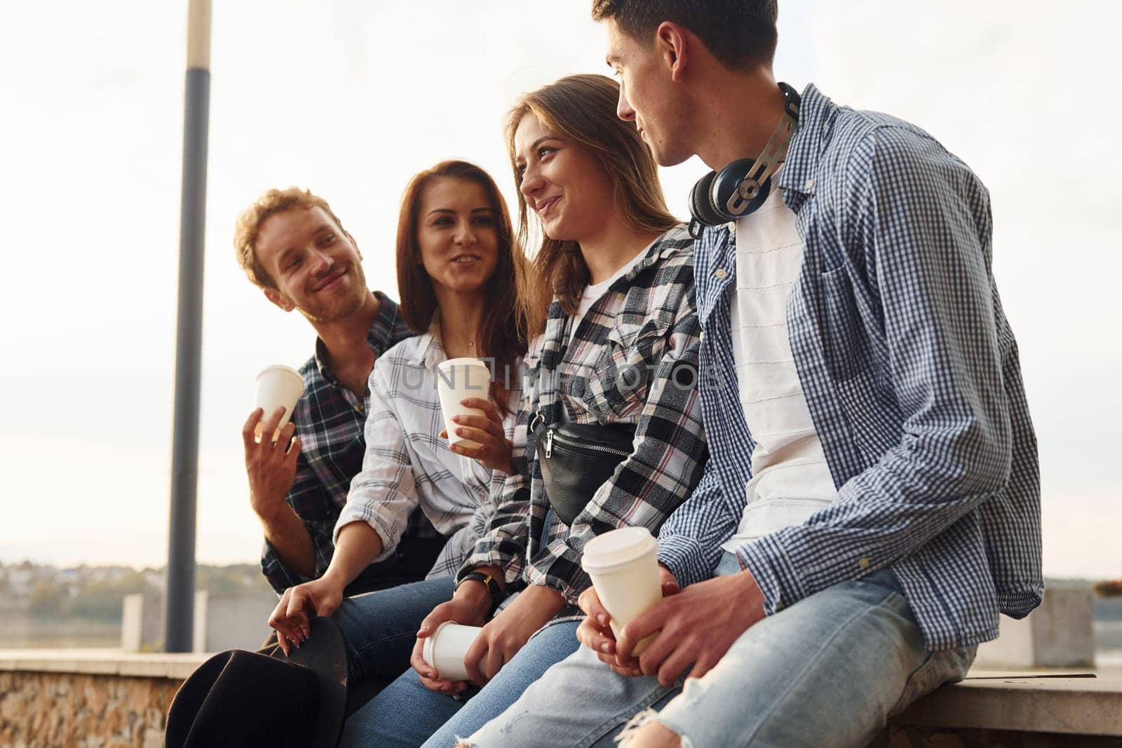 Sunny weather. Drinking coffee. Group of young cheerful friends that is outdoors having fun together.