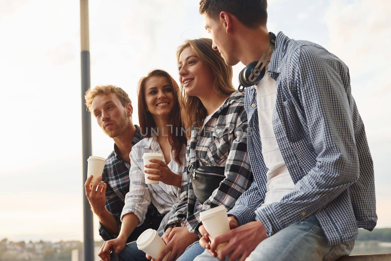 Sunny weather. Drinking coffee. Group of young cheerful friends that is outdoors having fun together.