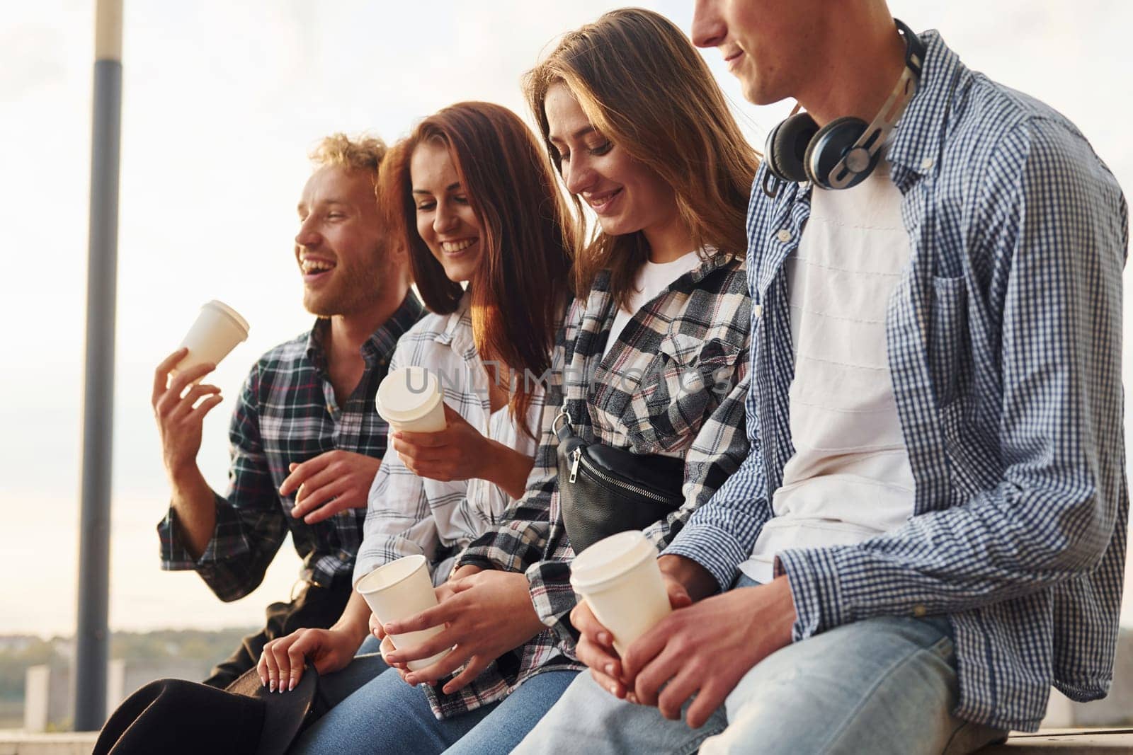 Sunny weather. Drinking coffee. Group of young cheerful friends that is outdoors having fun together.