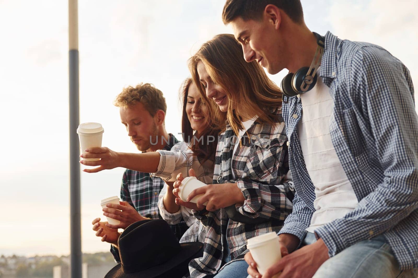 Sunny weather. Drinking coffee. Group of young cheerful friends that is outdoors having fun together.