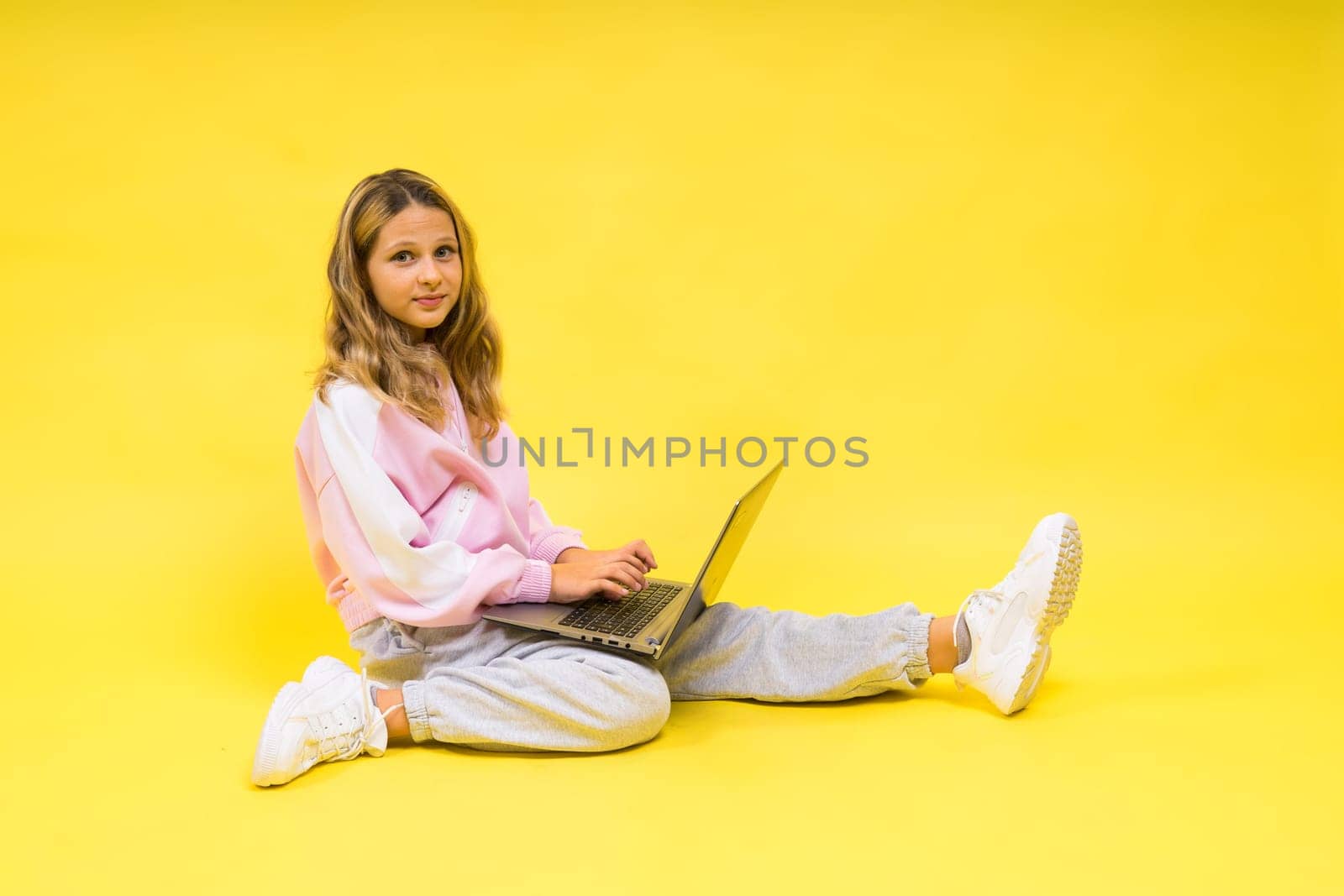 Positive kid sit with a laptop read homework wear casual style cloth isolated over yellow background