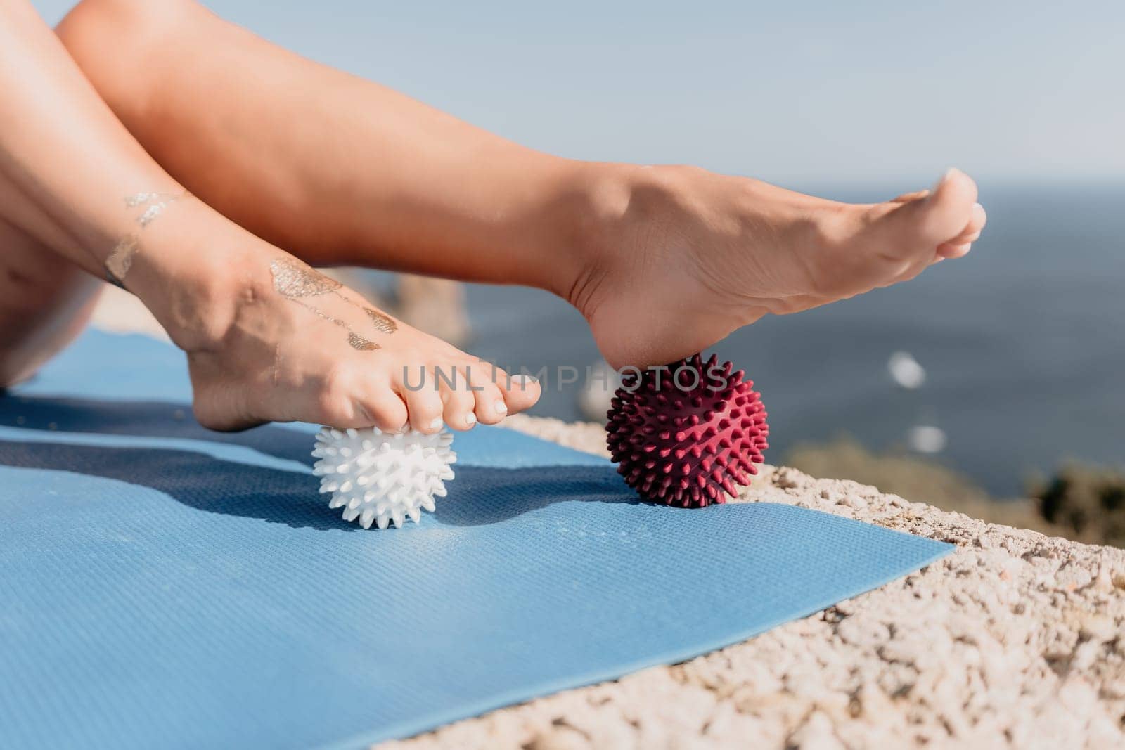 Middle aged well looking woman with black hair doing Pilates with the ring on the yoga mat near the sea on the pebble beach. Female fitness yoga concept. Healthy lifestyle, harmony and meditation.