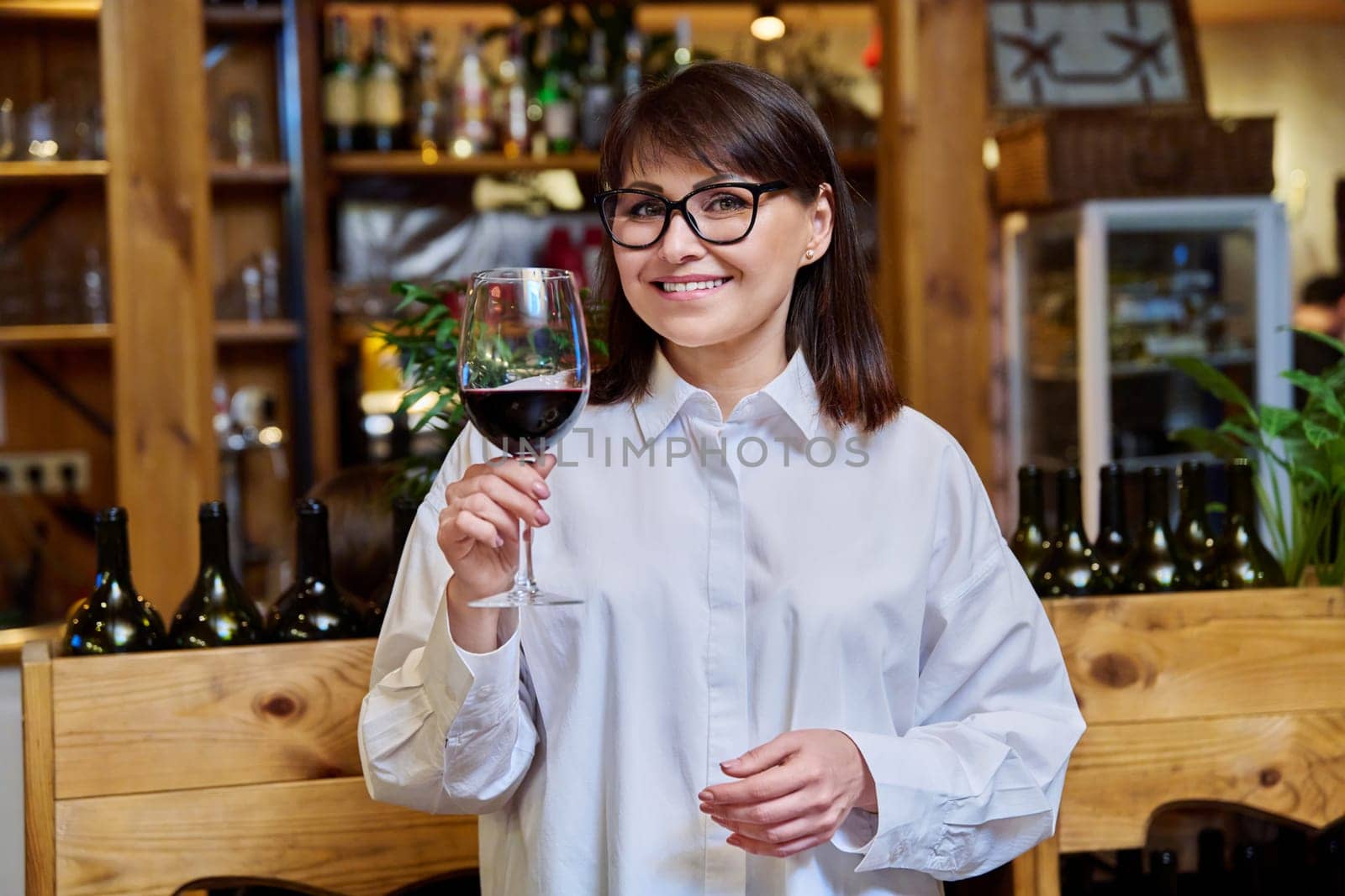Middle aged happy woman drinking glass of red wine in restaurant by VH-studio