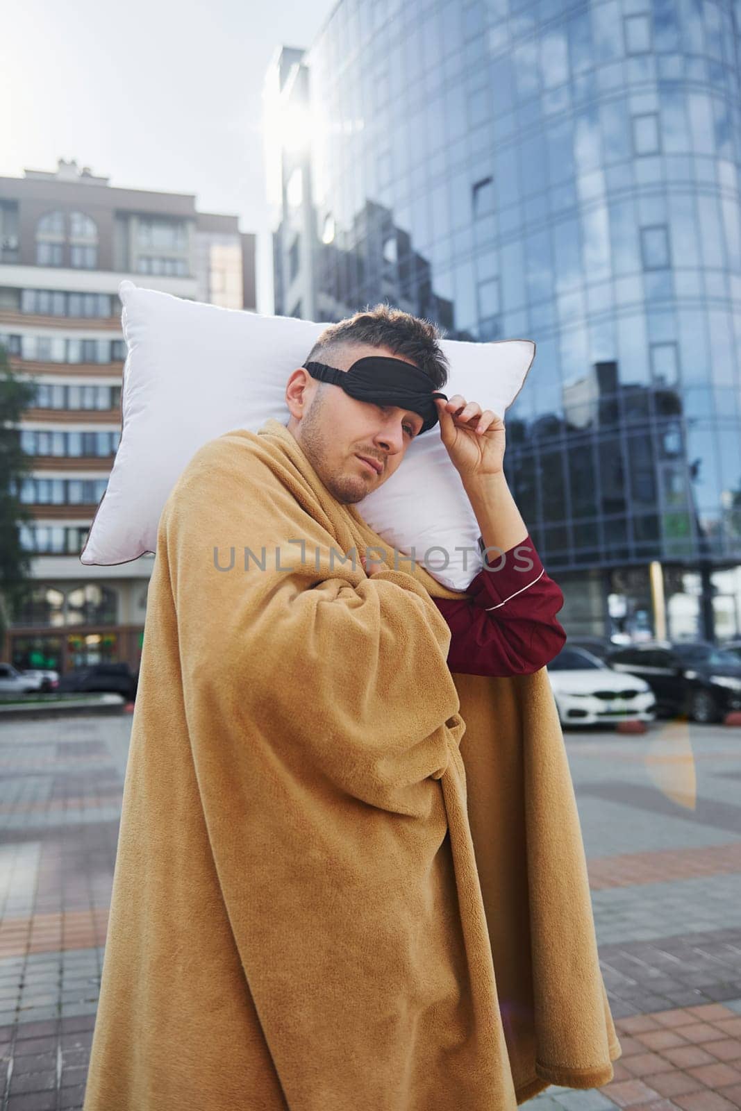 Against business building. Young man in pajama is outdoors on the street. Feels sleepy by Standret