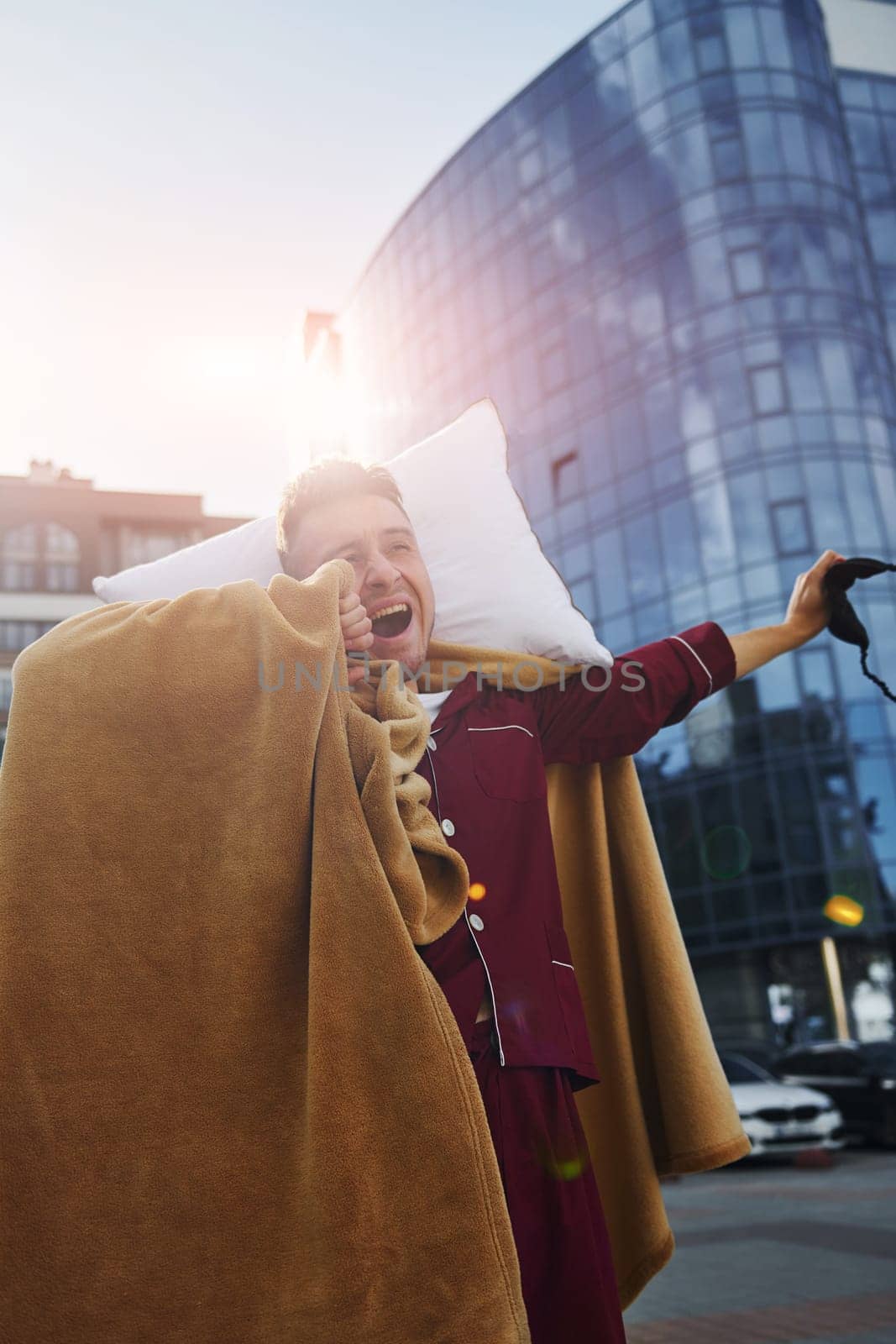 Against business building. Young man in pajama is outdoors on the street. Feels sleepy.