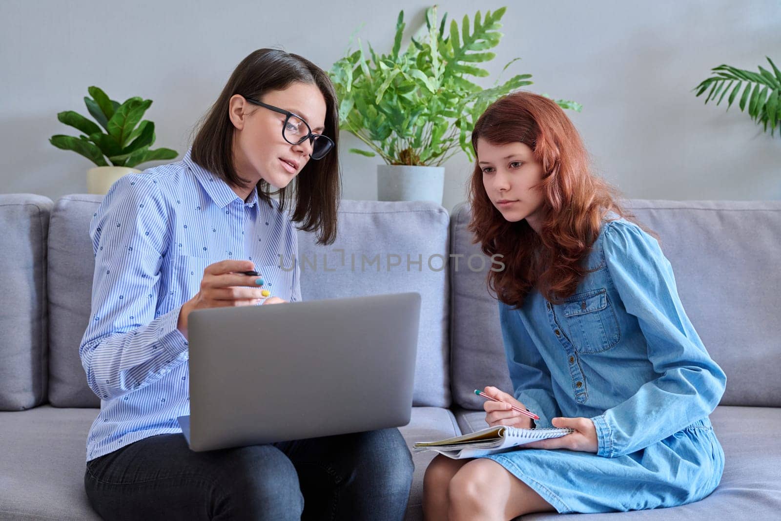 Preteen girl studying together with the teacher, in the office on the couch