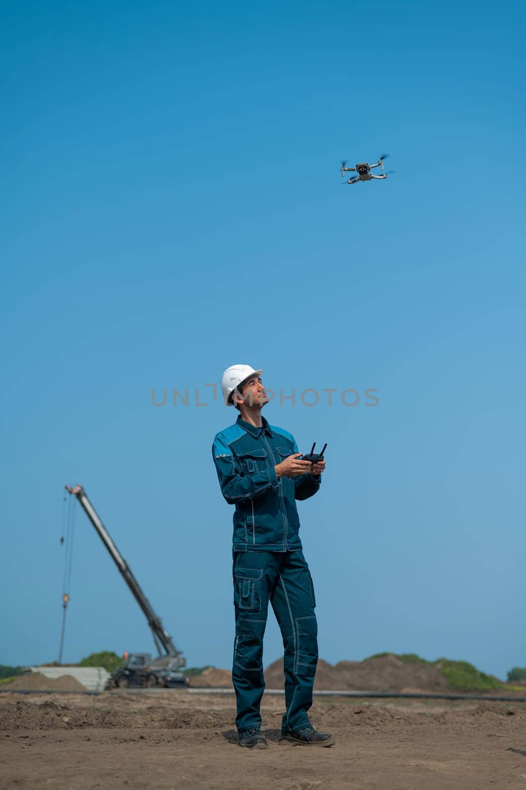 A man in a helmet and overalls controls a drone at a construction site. The builder carries out technical oversight. by mrwed54