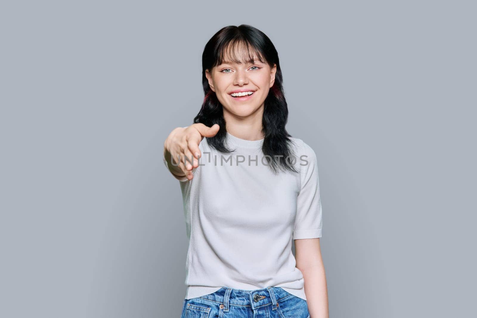 Young teenage female student shaking hands, over grey studio background. Meeting, welcome, greeting, contact, communication, youth concept