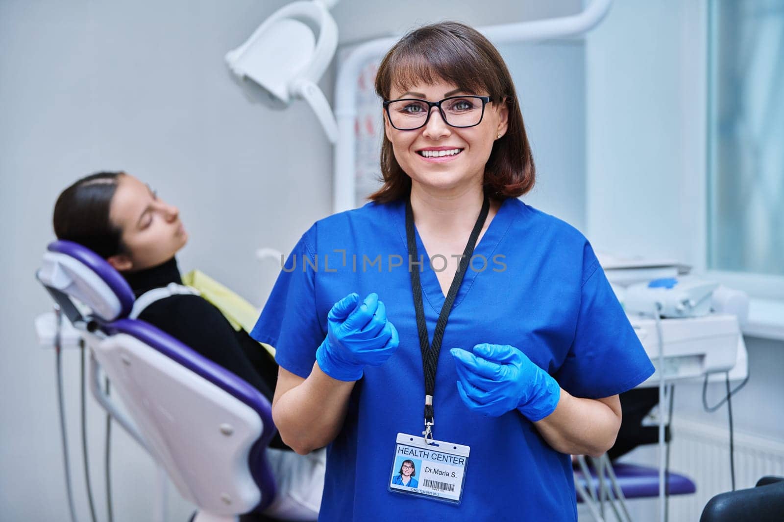 Portrait of smiling female dentist looking at camera with young girl patient sitting in dental chair. Visit to dentist examination treatment. Dentistry hygiene dental teeth health care concept