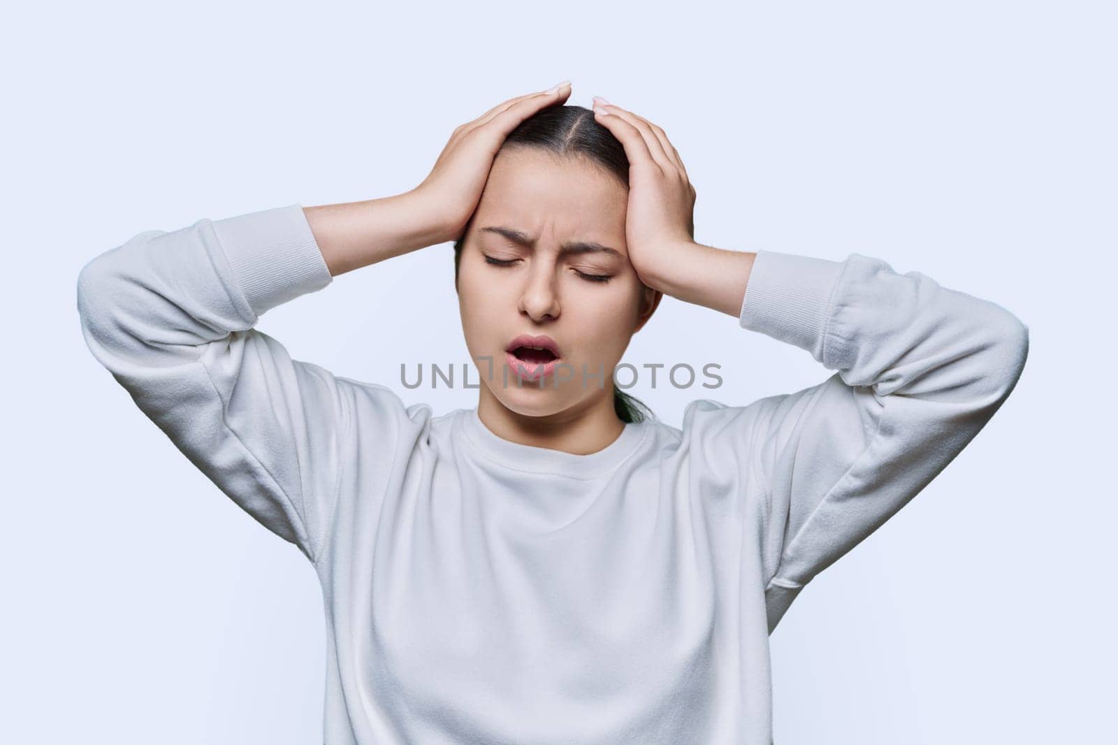 Shocked anxious young woman in panic holding her hands behind her head with her mouth open on white studio background. Teenage student with glasses in hysterics, shock stress helplessness anxiety