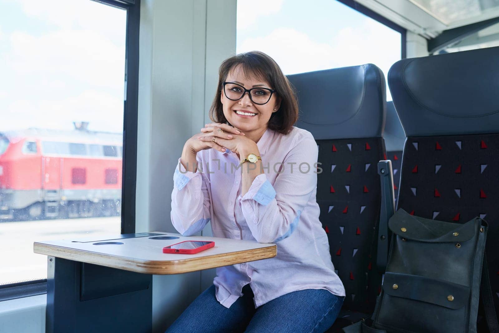 Woman sitting inside electric train, middle age female passenger smiling looking at camera. Transport, electric transport, railroad, people concept