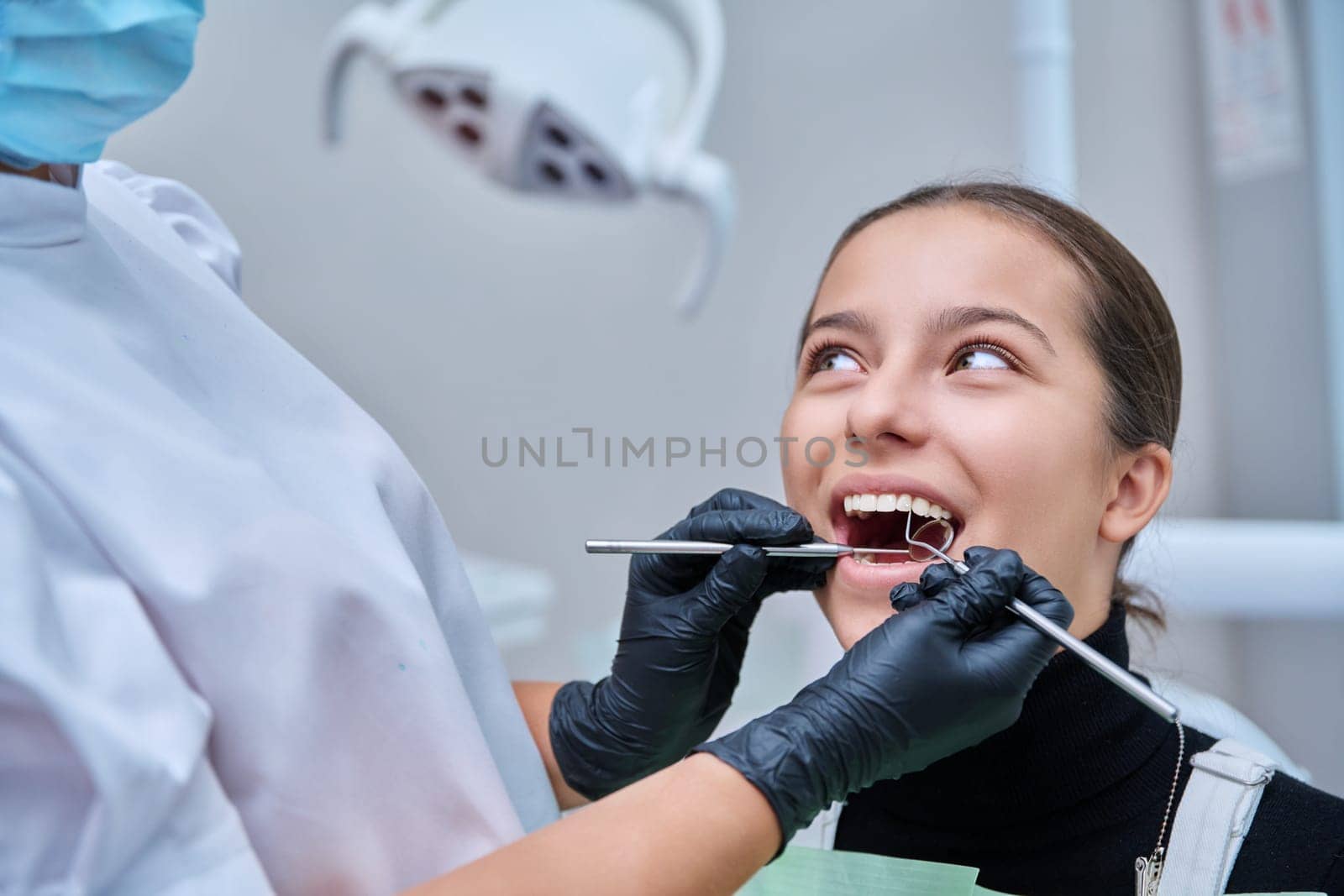 Young teenage female at dental checkup in clinic. Teenage girl sitting in chair, doctor dentist with tools examining patient's teeth. Adolescence, hygiene, dentistry, treatment, dental health care