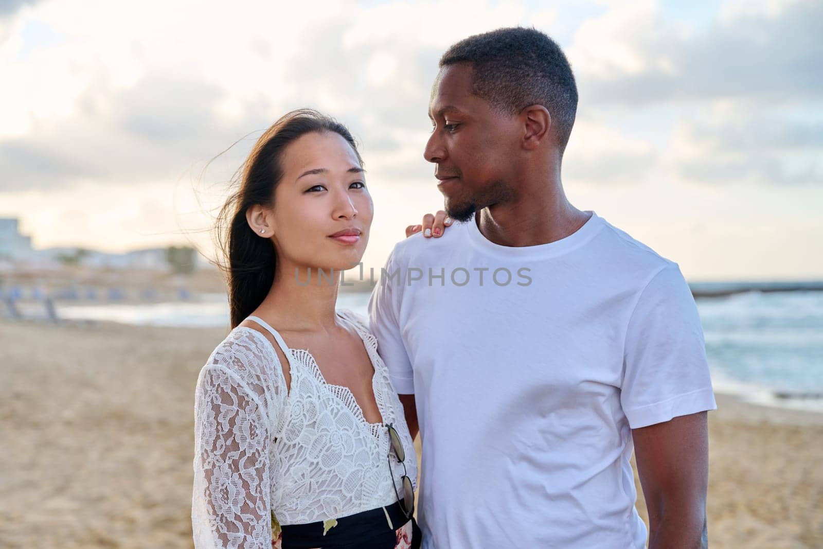 Young couple in love on the beach together. Multiethnic couple, asian woman and african american man. Love, honeymoon, relationship, lifestyle, togetherness, happiness, dating, multicultural family concept