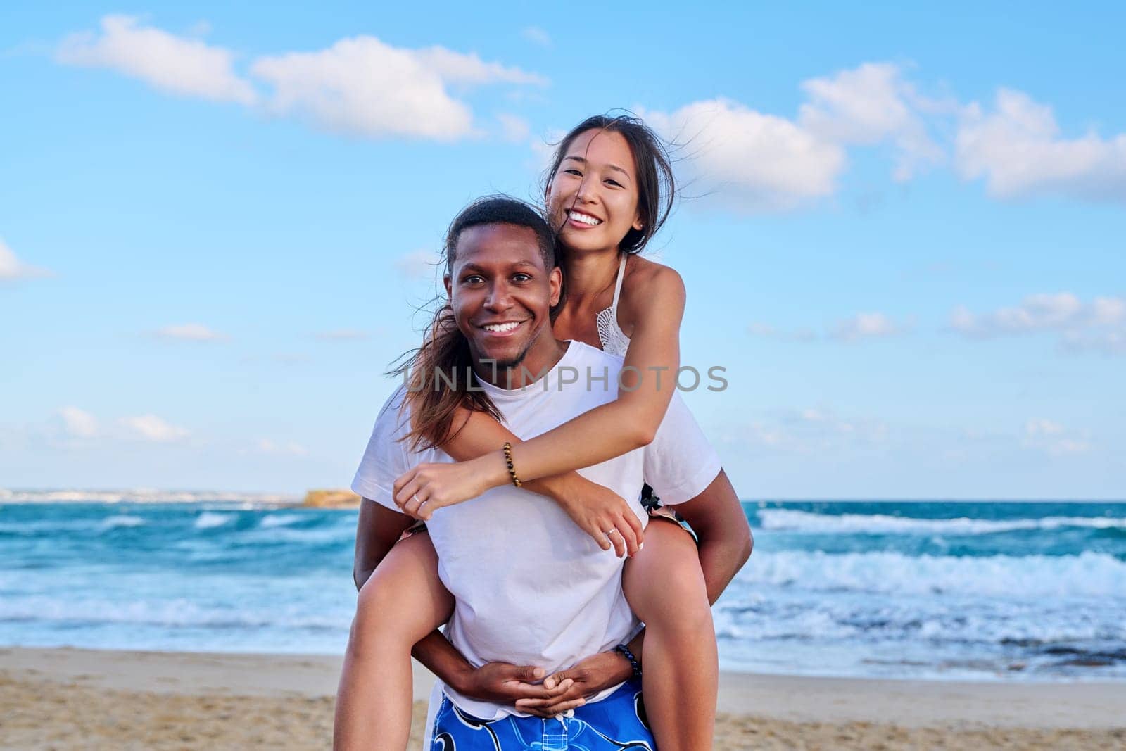 Happy young beautiful couple having fun on beach. Afro american asian couple laughing enjoying vacation in seaside nature. Multicultural, multiethnic family, relationships, togetherness, lifestyle